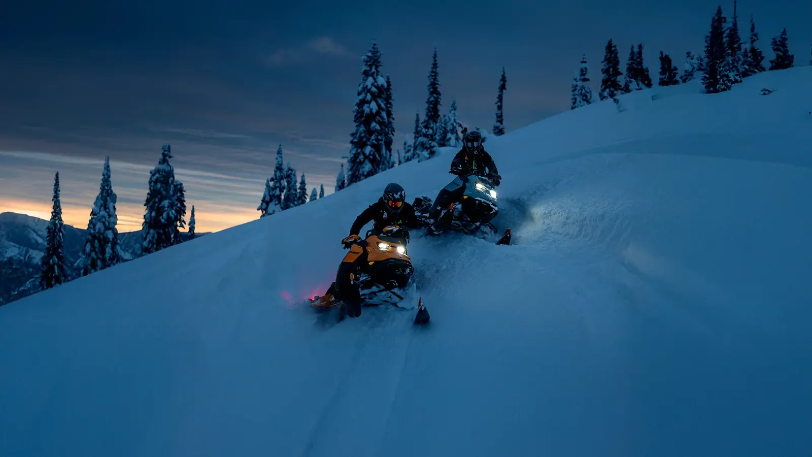 Två snöskotrar i djupsnö i skymningen